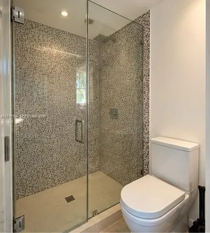 Walk-in shower featuring a frameless glass enclosure, floor-to-ceiling mosaic tile surround, rainfall showerhead, and a two-piece white toilet