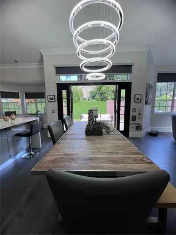 Modern multi-ring LED chandelier, dark wood-finish flooring, and black-framed French doors leading to exterior grounds
