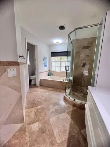 Bathroom featuring a corner glass-enclosed shower, stone-tile flooring, built-in soaking tub, and a vanity with a white countertop