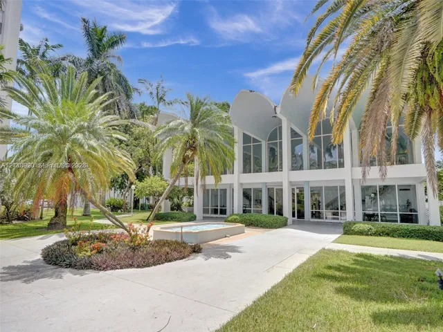 Mid-century modern exterior featuring dramatic vaulted rooflines, expansive floor-to-ceiling glass windows, concrete hardscaping, and established palm landscaping