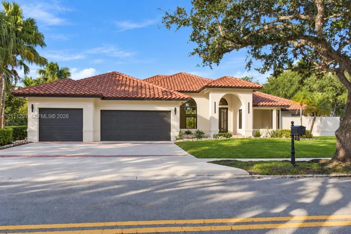 Stucco exterior featuring a terracotta tile roof, arched entryway, and three-car garage with paneled doors