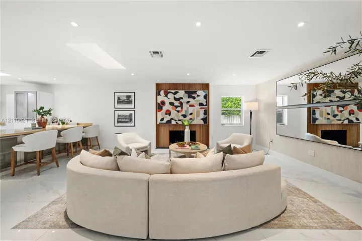 Open-concept living space featuring large-format tile flooring, a recessed skylight, recessed lighting, a wood-paneled fireplace surround, and extensive wall-mounted mirrors