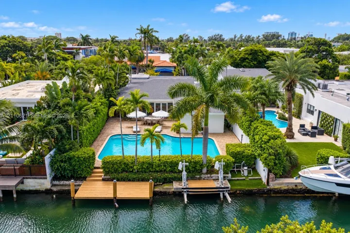 Waterfront property featuring a private swimming pool, a wood-finish dock, a boat lift, and lush landscaping