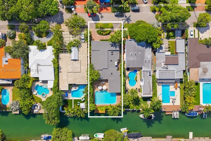 Waterfront property featuring a private swimming pool, paved patio, mature perimeter landscaping, and direct canal access