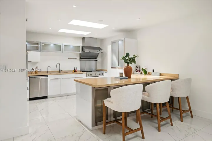 Kitchen featuring white flat-panel cabinetry, stainless steel appliances, solid surface countertops, a central island with integrated storage, and recessed ceiling lighting