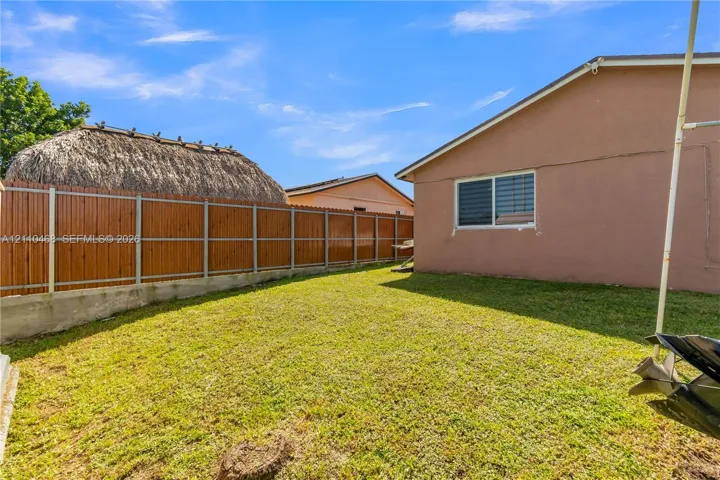 Rear yard featuring a manicured lawn, concrete retaining wall, and horizontal wood-panel fencing