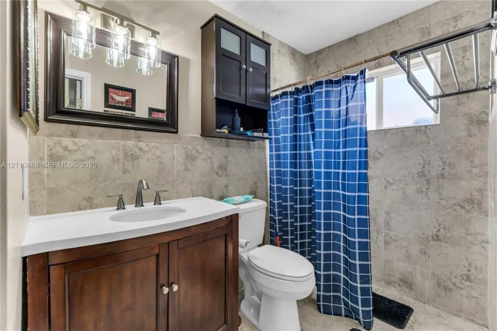 Bathroom featuring a wood-finish vanity with a white countertop, wall-mounted cabinetry, tile wall surfacing, and a three-light vanity fixture
