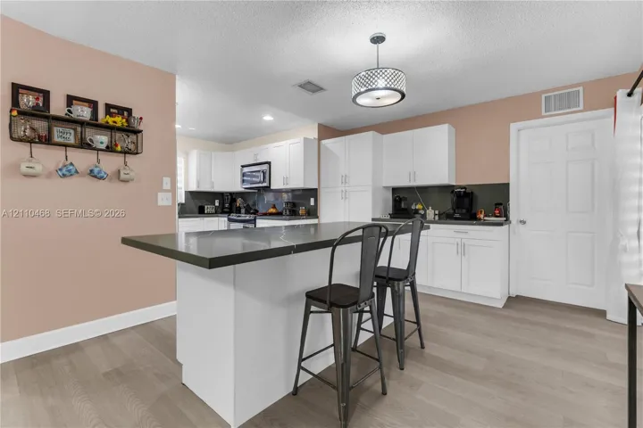 Kitchen featuring white shaker-style cabinetry, a central island with a dark countertop, wood-finish flooring, and a drum-style pendant light fixture