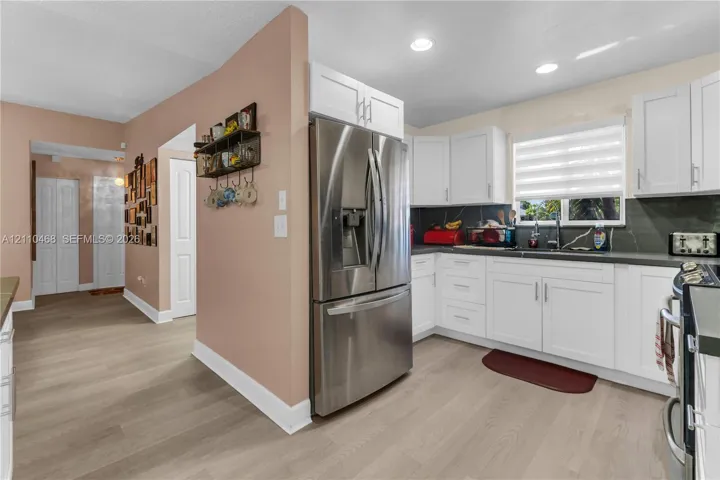 Kitchen featuring white shaker-style cabinetry, stainless steel refrigerator, dark countertops, wood-finish flooring, and recessed ceiling lighting