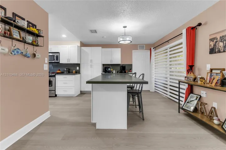Kitchen featuring white cabinetry, an island with a solid surface countertop, wood-finish flooring, and horizontal blind window coverings
