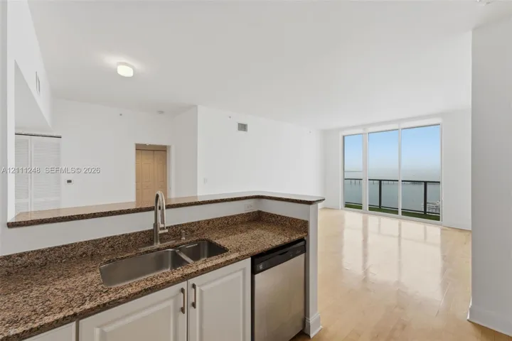 Kitchen featuring stone-finish countertops, stainless steel dual-basin sink, wood-finish flooring, and floor-to-ceiling glass panel windows