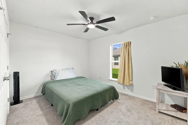Guest bedroom with ceiling fan and large window.