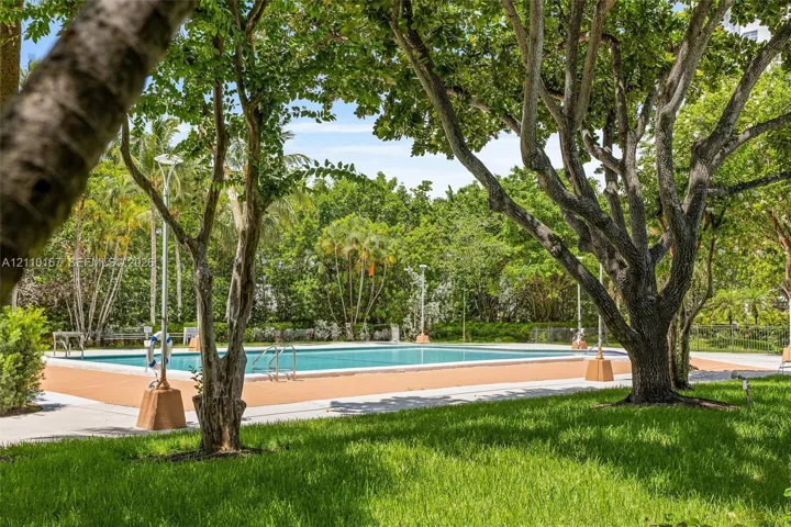Swimming pool with a solid-surface deck, surrounded by mature trees, landscaping, and integrated lighting fixtures