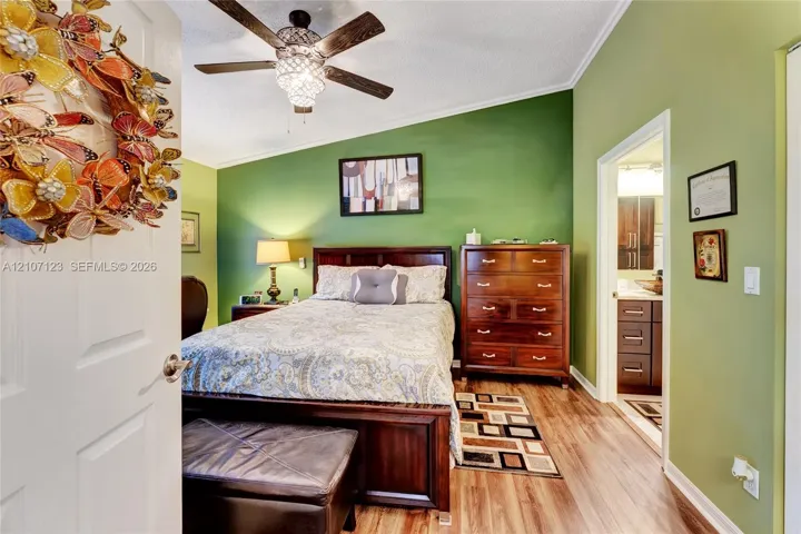 Sloped ceiling featuring a multi-blade ceiling fan with an integrated light fixture and wood-finish flooring