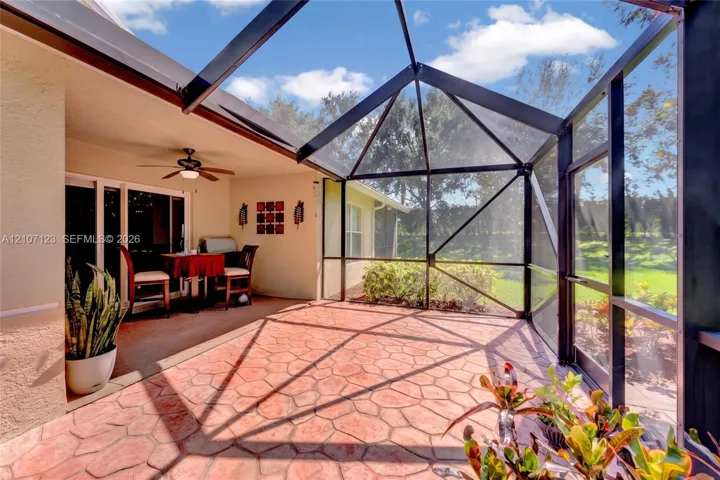 Screened-in lanai featuring a stamped concrete patio, vaulted structural framing, and a mounted ceiling fan