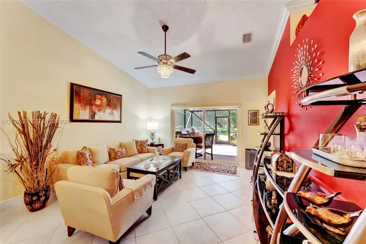 Living area featuring vaulted ceilings, crown molding, large-format tile flooring, a central ceiling fan with an integrated light fixture, and glass sliding doors