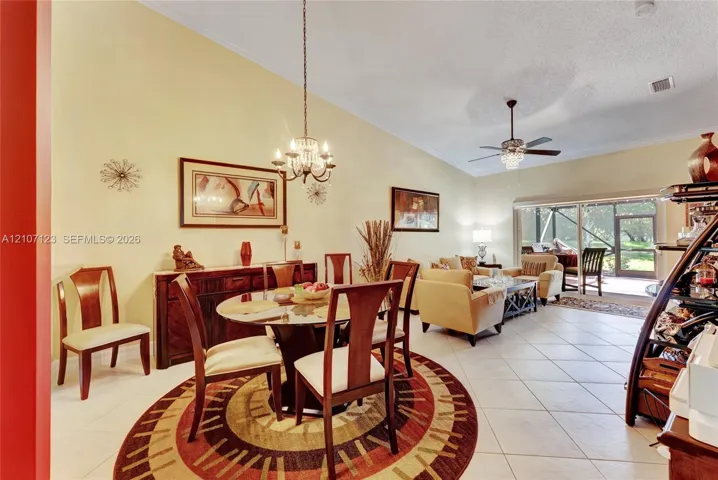 Vaulted ceilings featuring a chandelier, tile flooring, and sliding glass doors with a screen enclosure