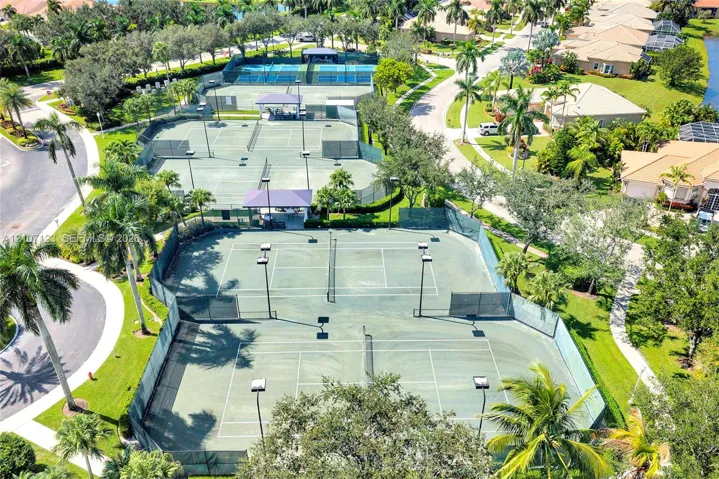 Multi-court tennis facility featuring hard-surface playing areas, fenced perimeters, overhead lighting, and covered spectator seating