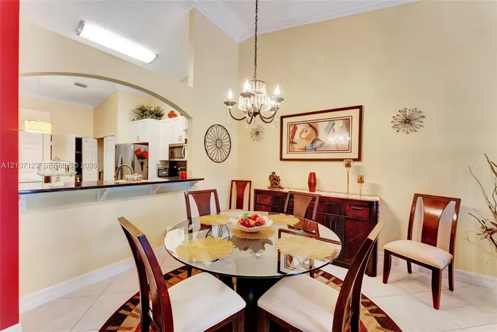 Dining area featuring vaulted ceilings, an arched wall opening, a decorative hanging chandelier, and neutral tile flooring