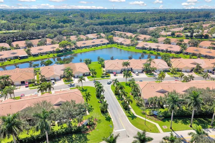 Aerial perspective of a residential community featuring a central lake, manicured lawns, mature palm trees, and paved street infrastructure