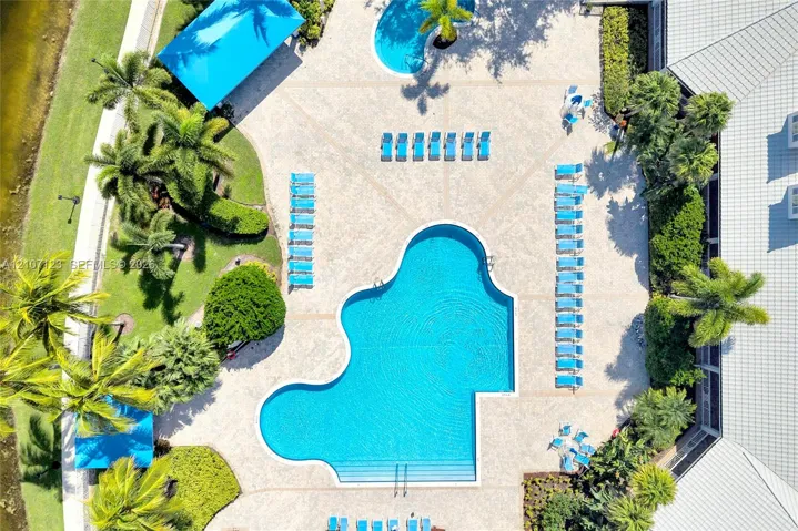Swimming pool with integrated stairs, expansive paver deck, dual covered shaded structures, and professional landscaping featuring mature palm trees