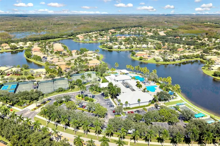 Aerial perspective of the property featuring a central clubhouse, multiple outdoor swimming pools, tennis courts, and surrounding water bodies