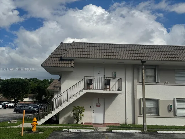 Multi-story exterior featuring a shingled roof, stucco siding, and an external metal staircase with matching railings