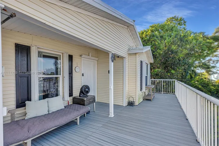 Covered deck featuring light-colored horizontal lap siding, white metal railings, black louvered window shutters, and wood-finish decking