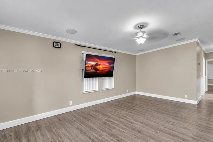Neutral-toned walls featuring crown molding, wood-finish flooring, ceiling fan with integrated lighting, and recessed ceiling speakers