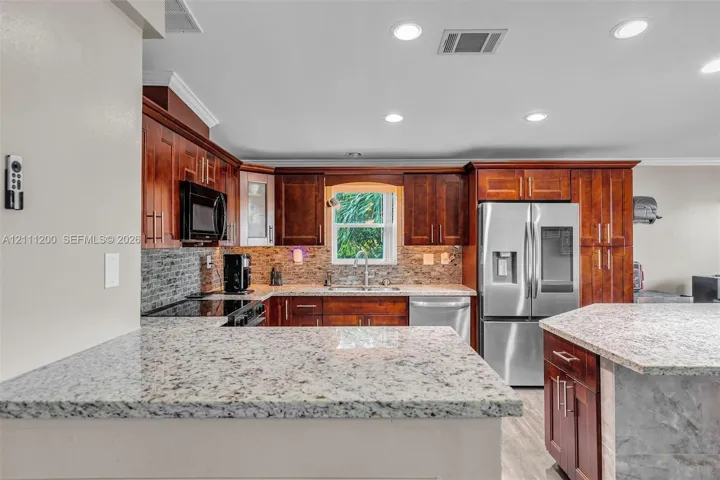 Kitchen featuring rich wood cabinetry, stone-surface countertops, stone tile backsplash, recessed ceiling lighting, and stainless steel appliances