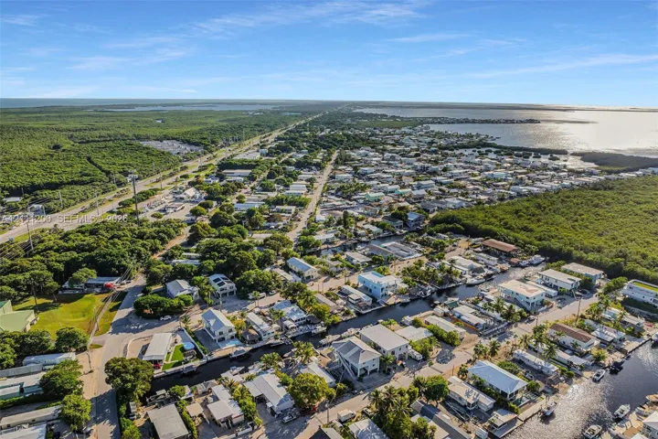 Aerial perspective of a coastal residential area featuring direct canal access, expansive water frontage, mature canopy trees, and proximity to regional waterways