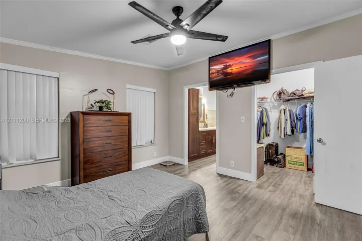 Wood-finish flooring, matte black ceiling fan with integrated lighting, dual windows with vertical blinds, and walk-in closet featuring built-in wire shelving