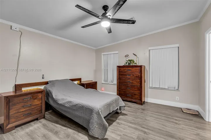 Wood-finish flooring, matte black ceiling fan with integrated lighting, dual windows with vertical blinds, and crisp crown molding