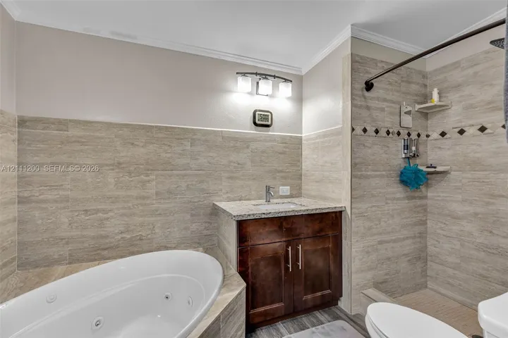 Bathroom featuring a jetted soaking tub, dark wood vanity with a stone countertop, and full-height wall tiling