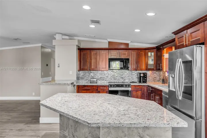 Kitchen featuring stained wood cabinetry, stone-finish countertops, tiled backsplash, stainless steel appliances, and a central island