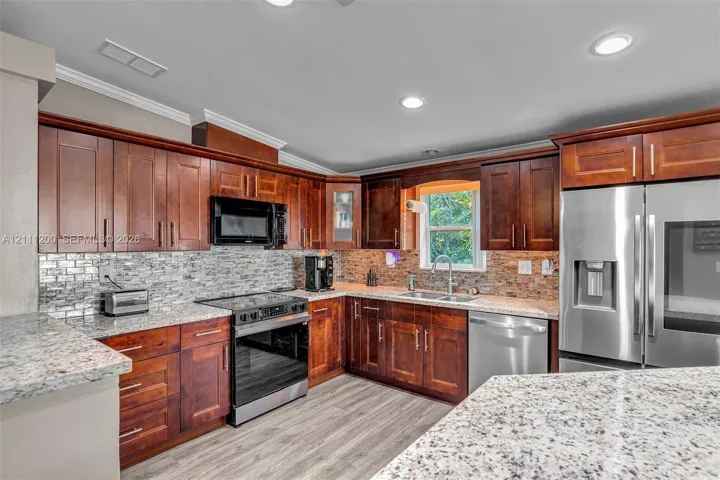 Kitchen featuring cherry-finish cabinetry, stone-pattern countertops, stainless steel appliances, a subway-style tile backsplash, and wood-finish flooring