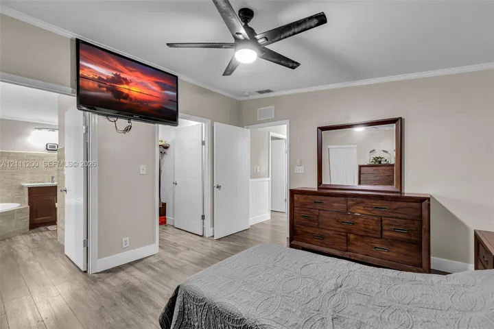 Room featuring wood-finish flooring, a five-blade ceiling fan with integrated lighting, and crown molding