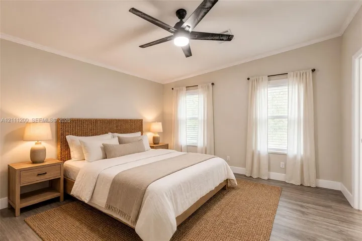 AI Generated Neutral-toned interior featuring wood-finish flooring, dual windows with curtain rods, and a ceiling fan with integrated lighting