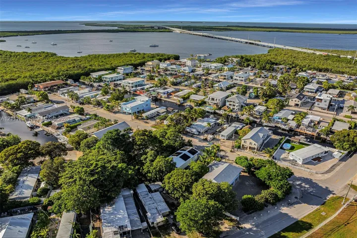 Aerial perspective of a coastal community featuring waterfront proximity, dense mature trees, and local infrastructure