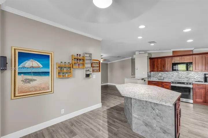 Kitchen featuring wood-finish cabinetry, stone-texture island countertop with a stone-tile base, stone-tile backsplash, and recessed ceiling lighting