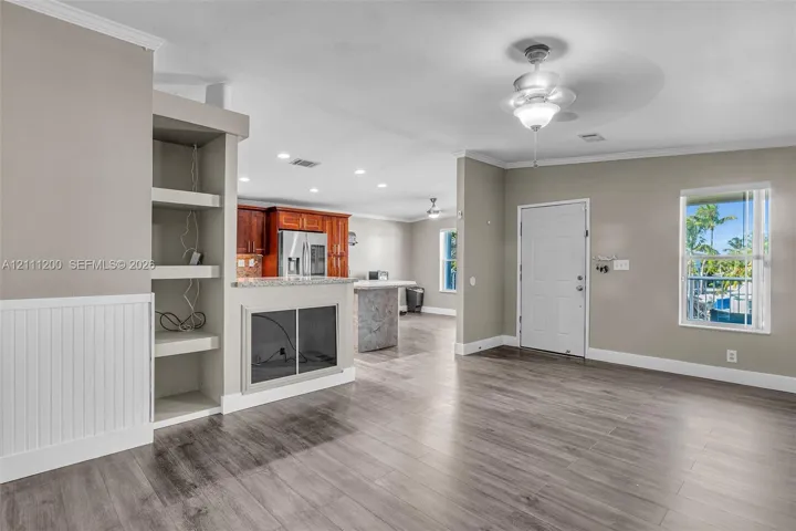 Open-concept interior featuring wood-finish flooring, built-in shelving, a kitchen island with stone countertops, and a ceiling fan with integrated lighting