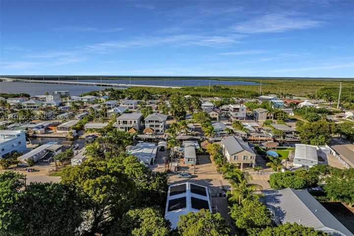 Aerial perspective featuring coastal surroundings, mature tropical vegetation, paved streets, and proximity to open water and causeway infrastructure