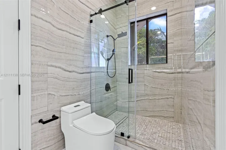 Walk-in shower featuring large-format horizontal tile, glass enclosure with matte black hardware, rainfall showerhead, and mosaic tile flooring
