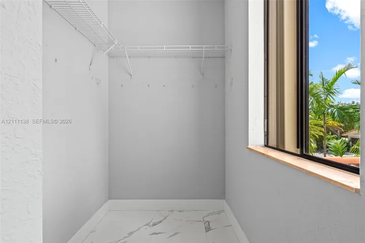 Storage area featuring white wire shelving, light-toned stone-finish tile flooring, and a window with a wood-finish sill