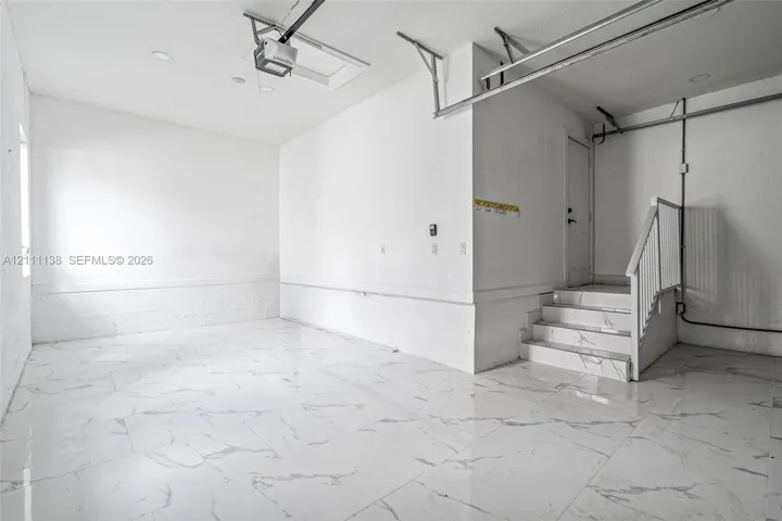 Finished garage space featuring large-format tile flooring, a staircase with matching tile risers and treads, recessed lighting, and white wall finishes