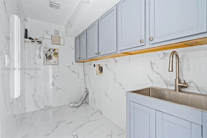 Utility area featuring floor-to-ceiling large-format stone-finish wall tile, light blue shaker-style cabinetry, a stainless steel basin sink, and a gooseneck faucet