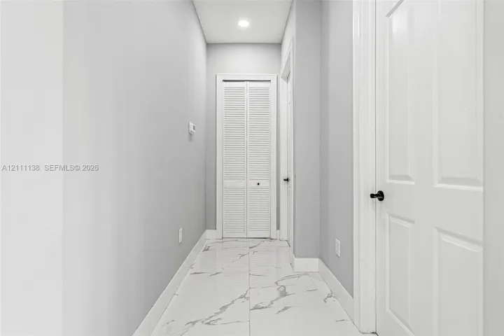 Hallway featuring polished tile flooring with a veined pattern, recessed ceiling lighting, and crisp white interior doors with matte black hardware