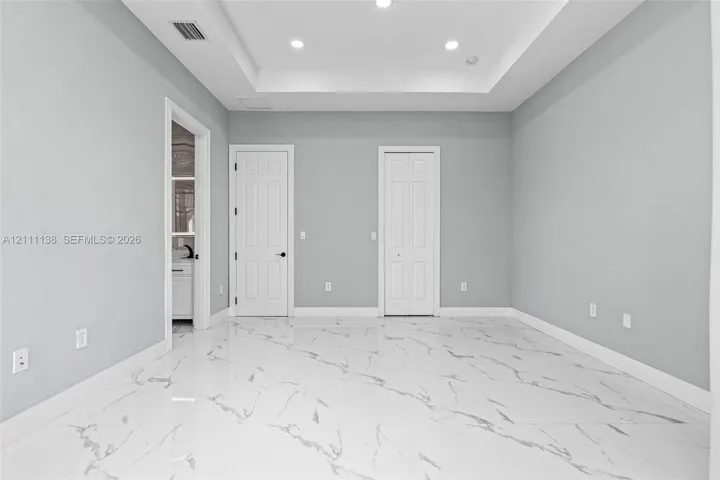 Interior space featuring a recessed tray ceiling, large-format stone-patterned tile flooring, and integrated recessed lighting