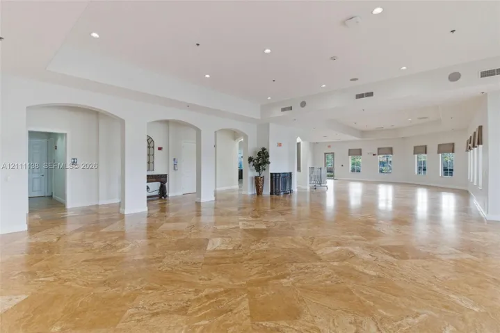 Expansive interior featuring large-format stone flooring, recessed ceiling lighting, multiple architectural archways, and oversized windows