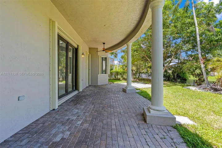 Covered curved patio featuring brick pavers, classical columns, and a ceiling-mounted fan